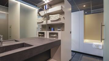 A modern bathroom with a large sink, built-in shelves with towels, a mirror, and a shower area.