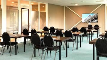 A conference room with multiple tables and chairs, a large screen on the wall, and a view of a building outside.