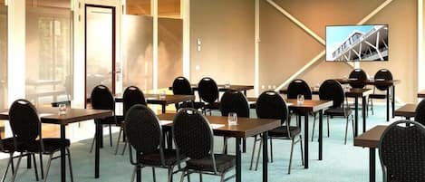 A conference room with multiple tables and chairs, a large screen on the wall, and a view of a building outside.
