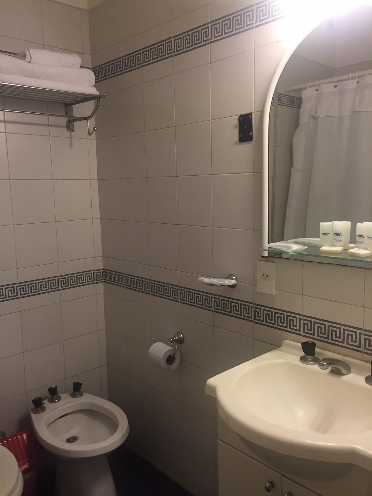 A bathroom with a bidet, toilet, sink, and a mirror with a shower curtain reflection.