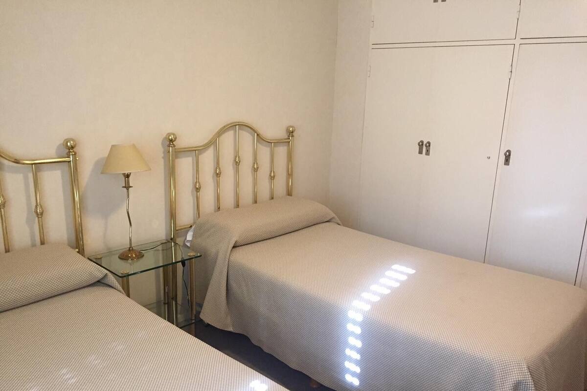 Quarto com duas camas de solteiro, uma mesa de cabeceira com abajur e um guarda-roupa de duas portas.