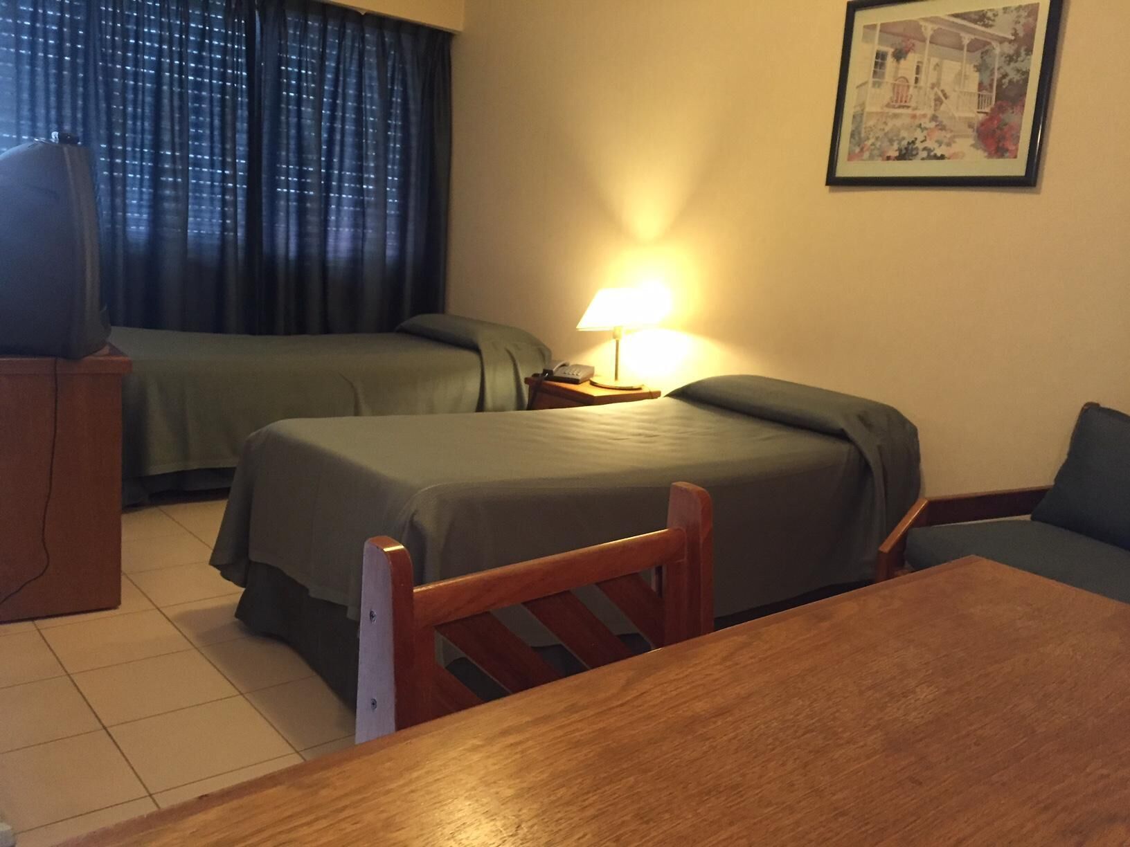 Ein Hotelzimmer mit zwei Betten, einem Schreibtisch, einem Sessel, einer Lampe und einem gerahmten Bild an der Wand.