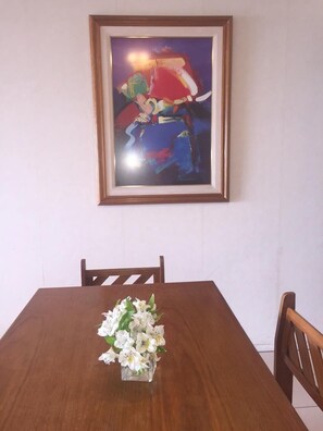 A dining table with a vase of white flowers and a framed abstract painting above it. - Apart Avenida del Mar (Mar del Plata)
