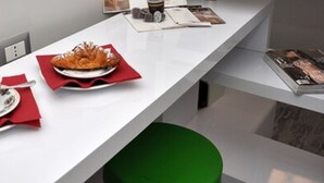 Una habitación de hotel moderna con un mostrador de recepción blanco, una silla verde y un croissant en un plato.