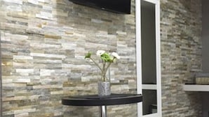 Un baño moderno con pared de mosaico de piedra, una mesa negra redonda con un florero y un espejo blanco, además de un taburete de madera.