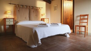 A bedroom with a large bed, two bedside tables with lamps, a wooden chair, and a wooden door. - B&B Molenda (Città di Castello)