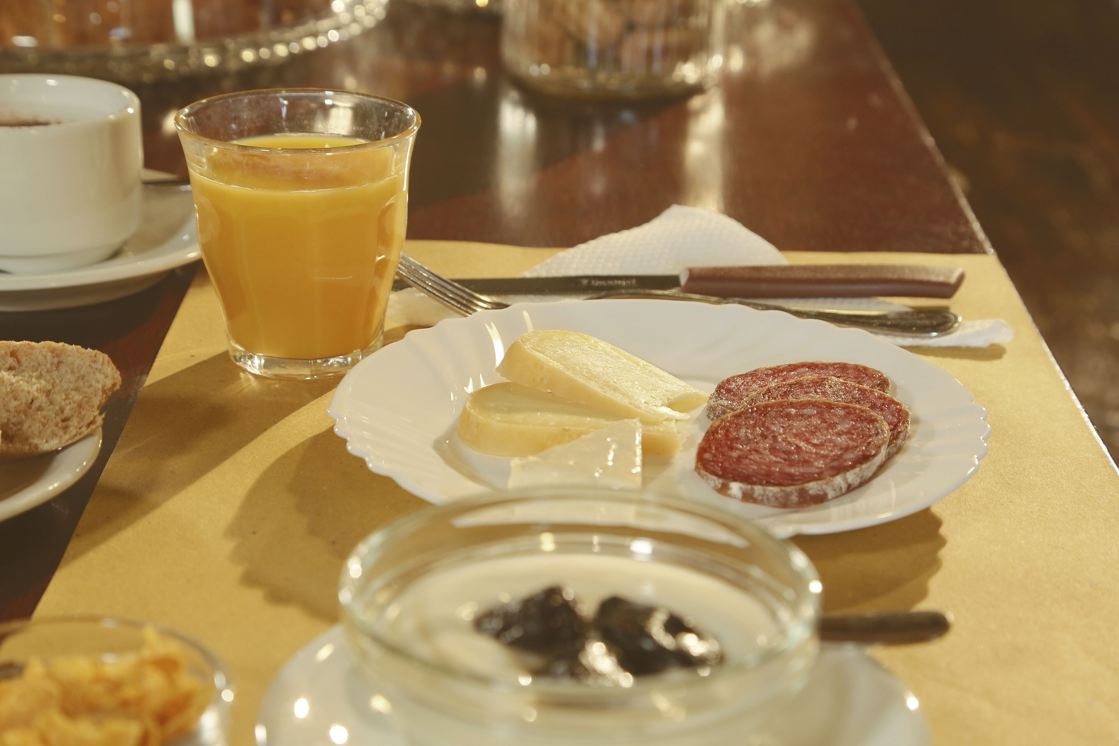 Une table mise pour le petit-déjeuner avec un verre de jus d’orange, une assiette contenant une tranche de banane, une tranche de jambon et un bol de mûres.