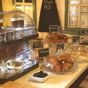 Ett bageridisplay med olika sorters bakverk och desserter, inklusive croissanter och tårtor, och med etiketter på italienska.