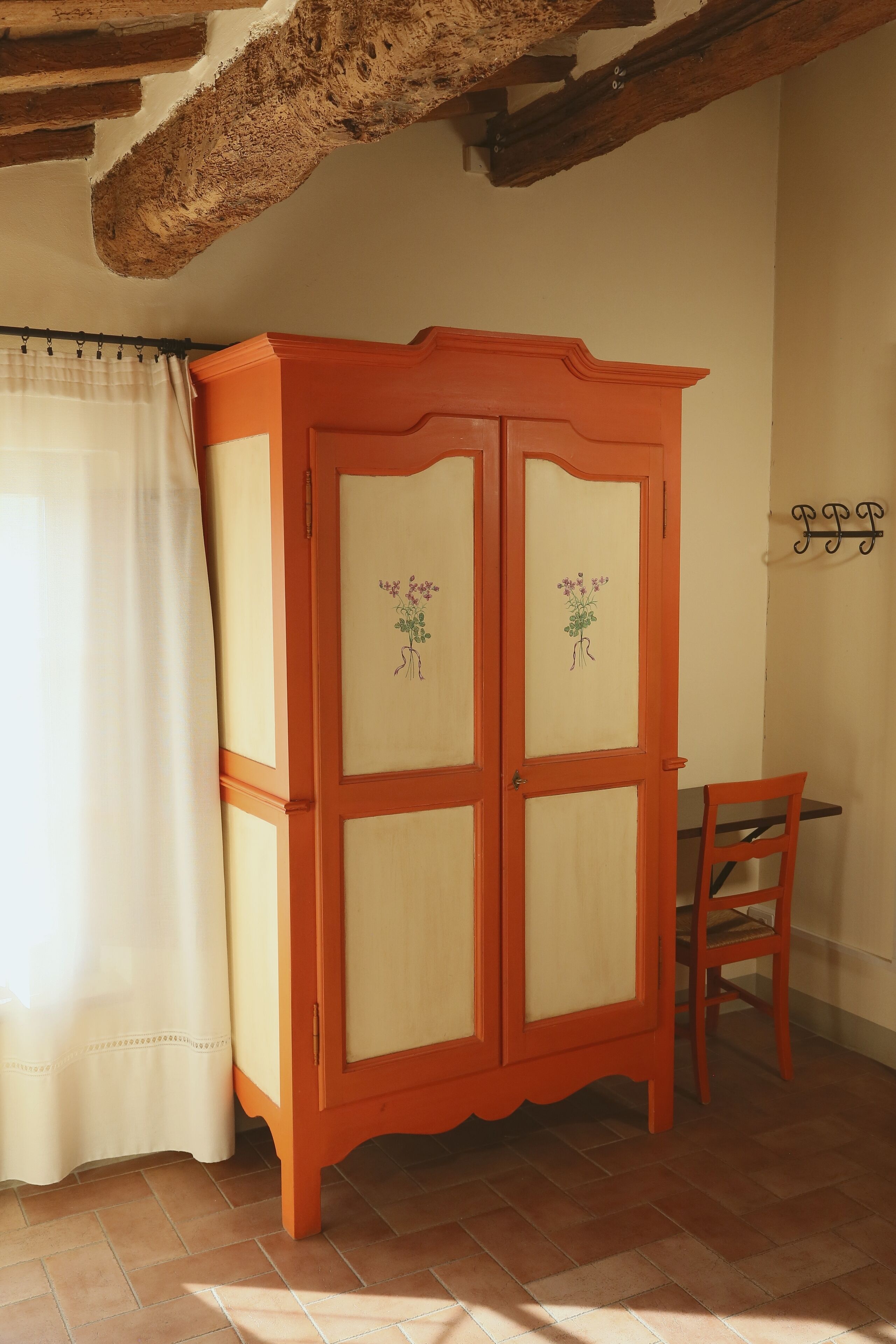 A room with a wooden cabinet with floral designs, a chair, and a curtain.