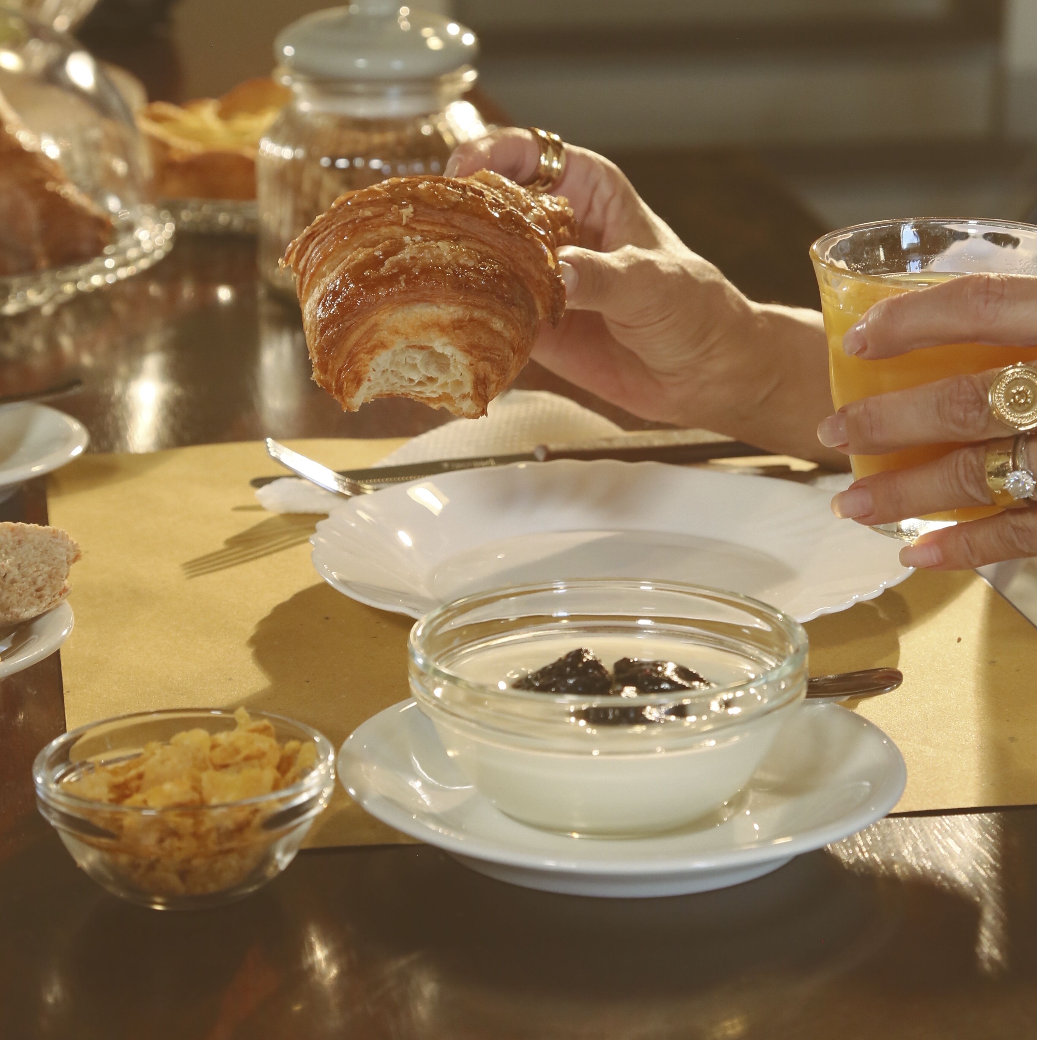 Una mesa con un croissant, un vaso de jugo y un bol de sopa.