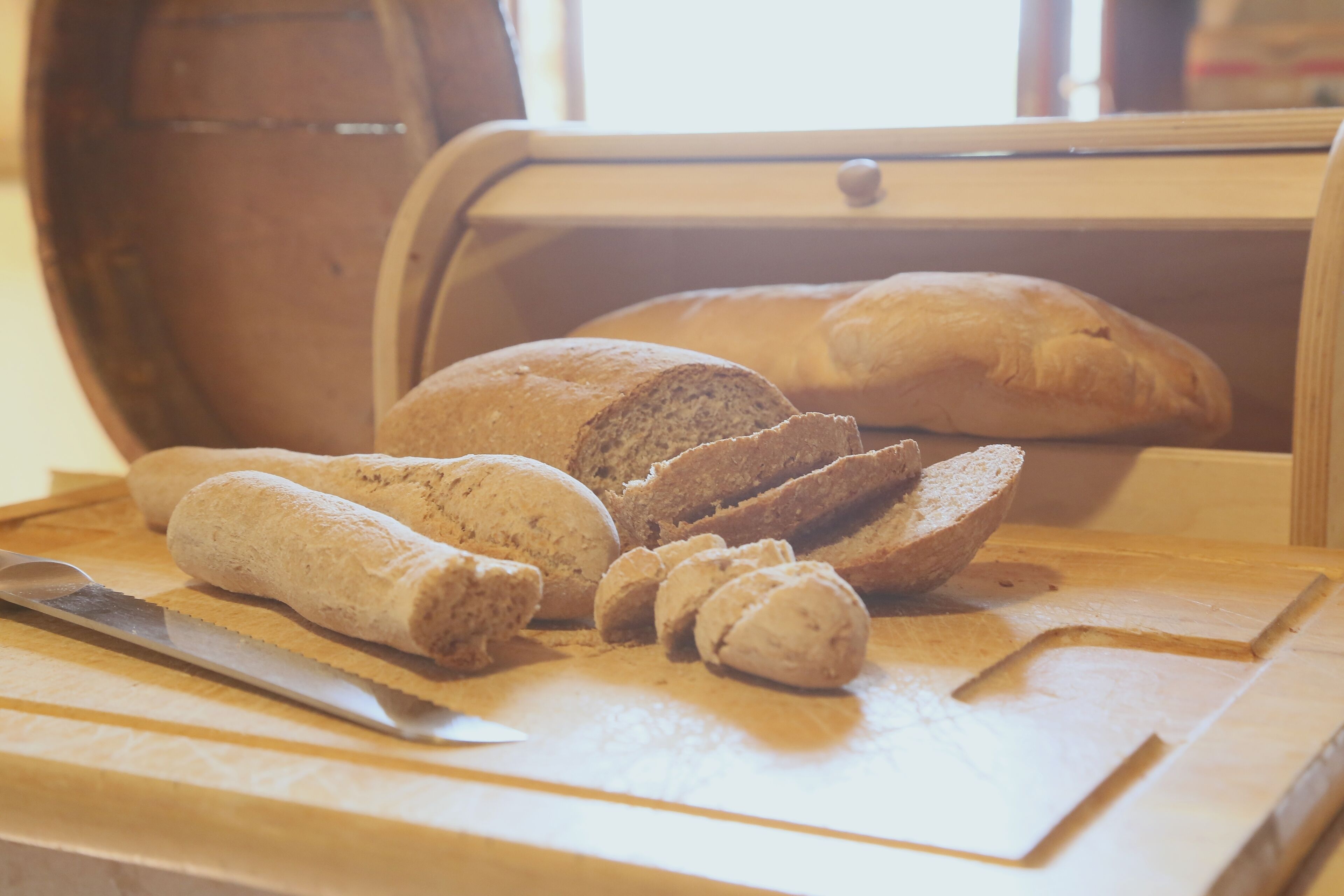 A wooden cutting board with sliced bread and a knife on a table.