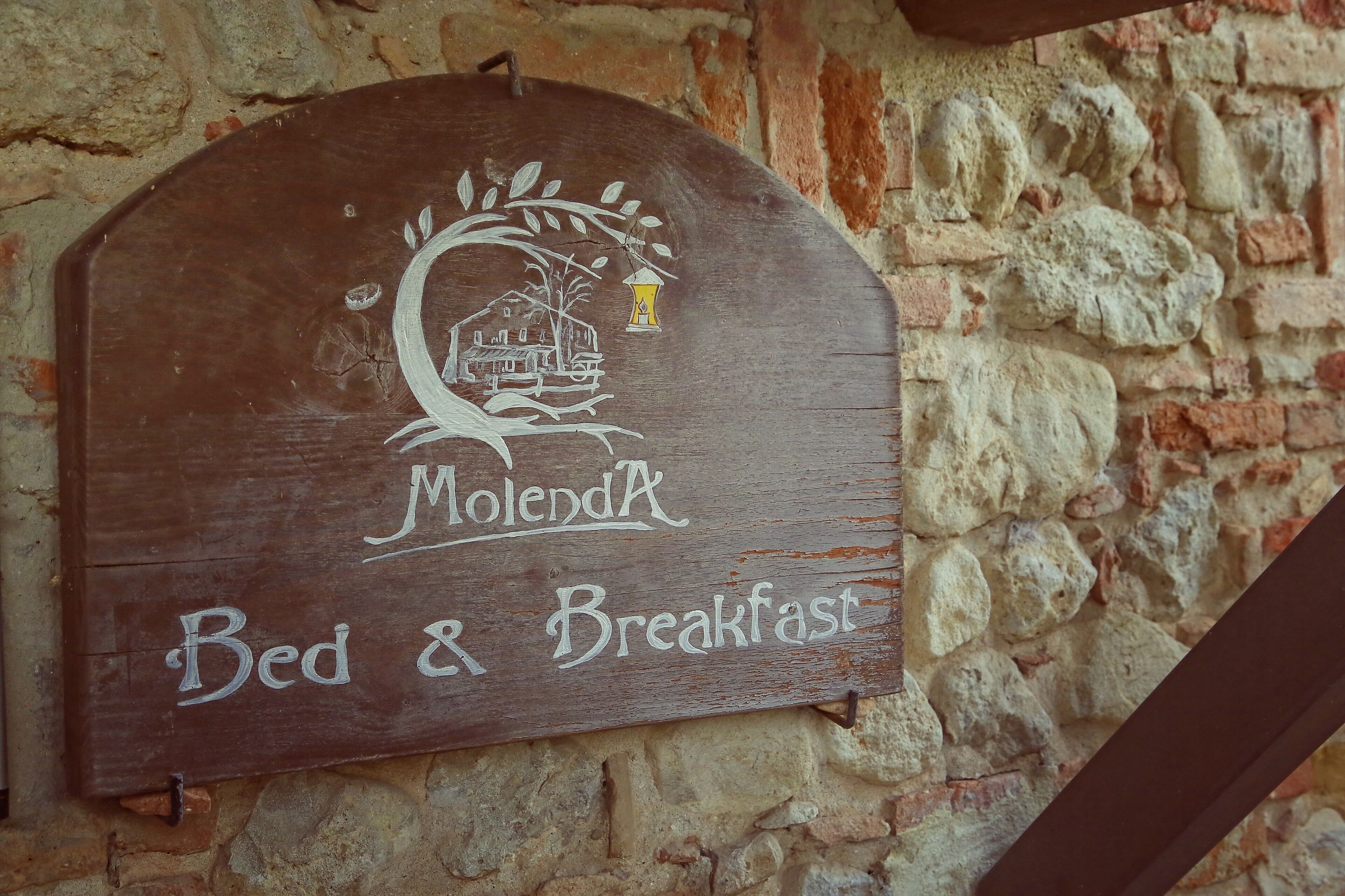 Een houten bord met een afbeelding van een huis en lantaarn, met de tekst 'Molenda Bed & Breakfast'.
