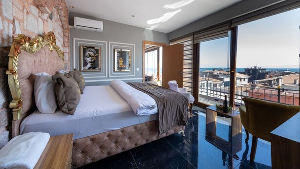 A modern bedroom with a large bed, a view of the city, and a balcony with a table and chair. - Holiday Business Otel (Istanbul)