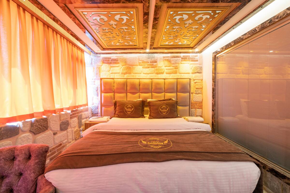Ein Hotelzimmer mit Steingemäuer, einem Bett mit Kopfteil und einem Fenster mit Vorhängen.