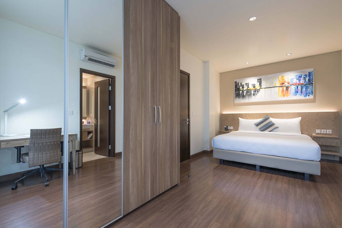 Una habitación de hotel moderna con una cama grande, un escritorio y una pintura de un paisaje urbano sobre la cama.