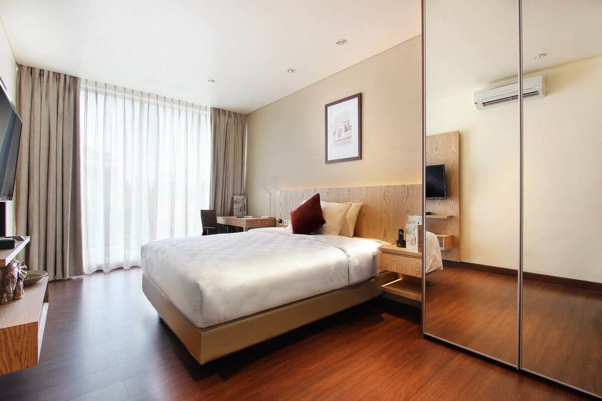 Una habitación de hotel con una cama grande, un escritorio con silla, un televisor y un espejo.