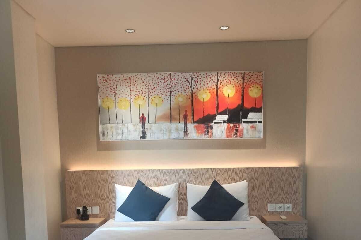 Une chambre d’hôtel avec un grand lit, deux tables de chevet, un tableau au-dessus du lit et un plancher en bois.