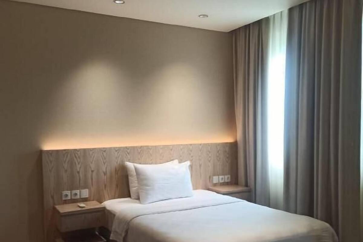 Una habitación de hotel con cama, mesitas de noche y un velador.