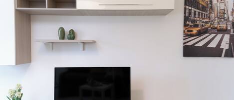 Een moderne woonkamer met een flatscreen televisie, een inbouwplank met decoratieve planten en een stadsgezicht schilderij aan de muur.