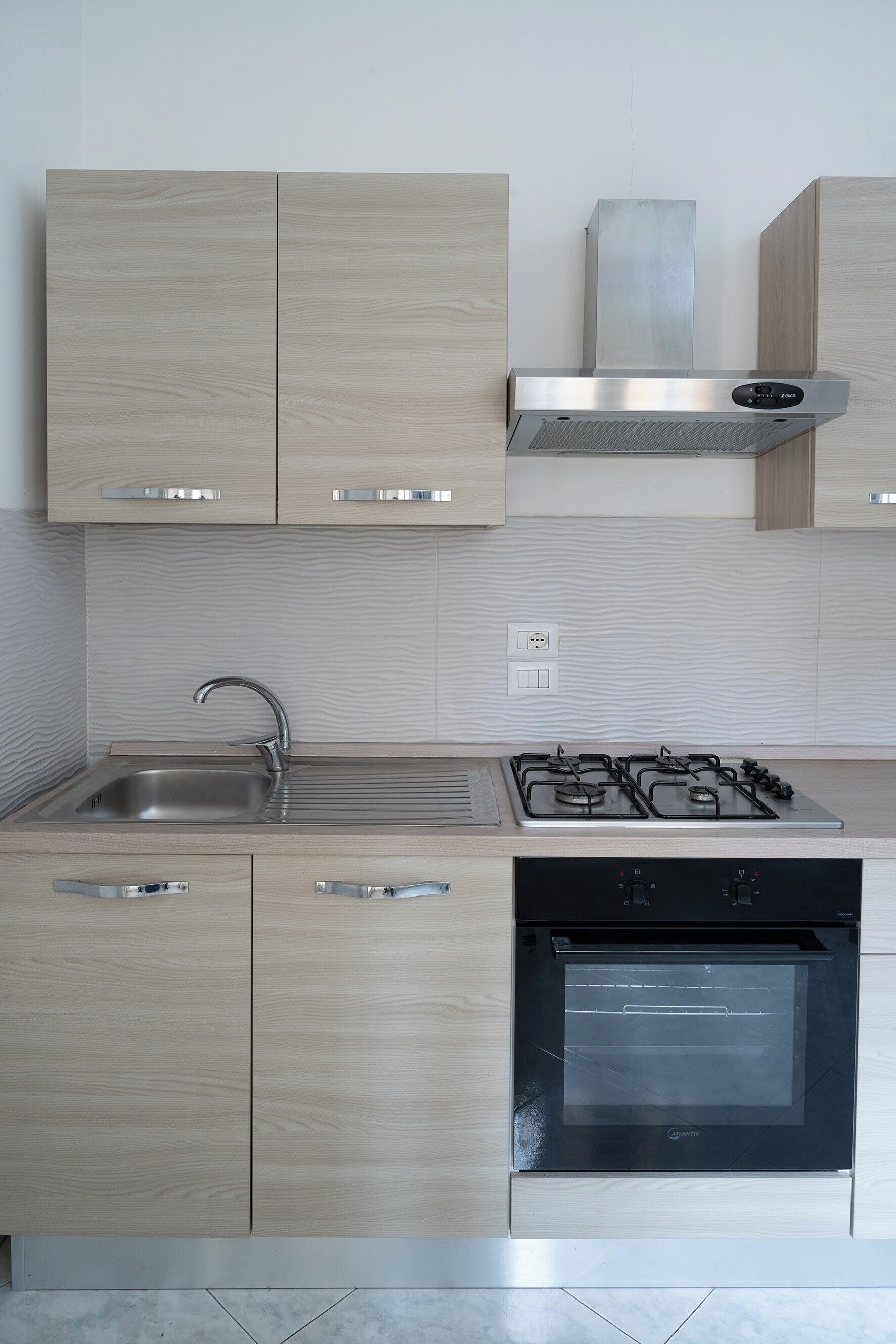 A modern kitchen with light wood cabinetry, stainless steel appliances, and a built-in oven.