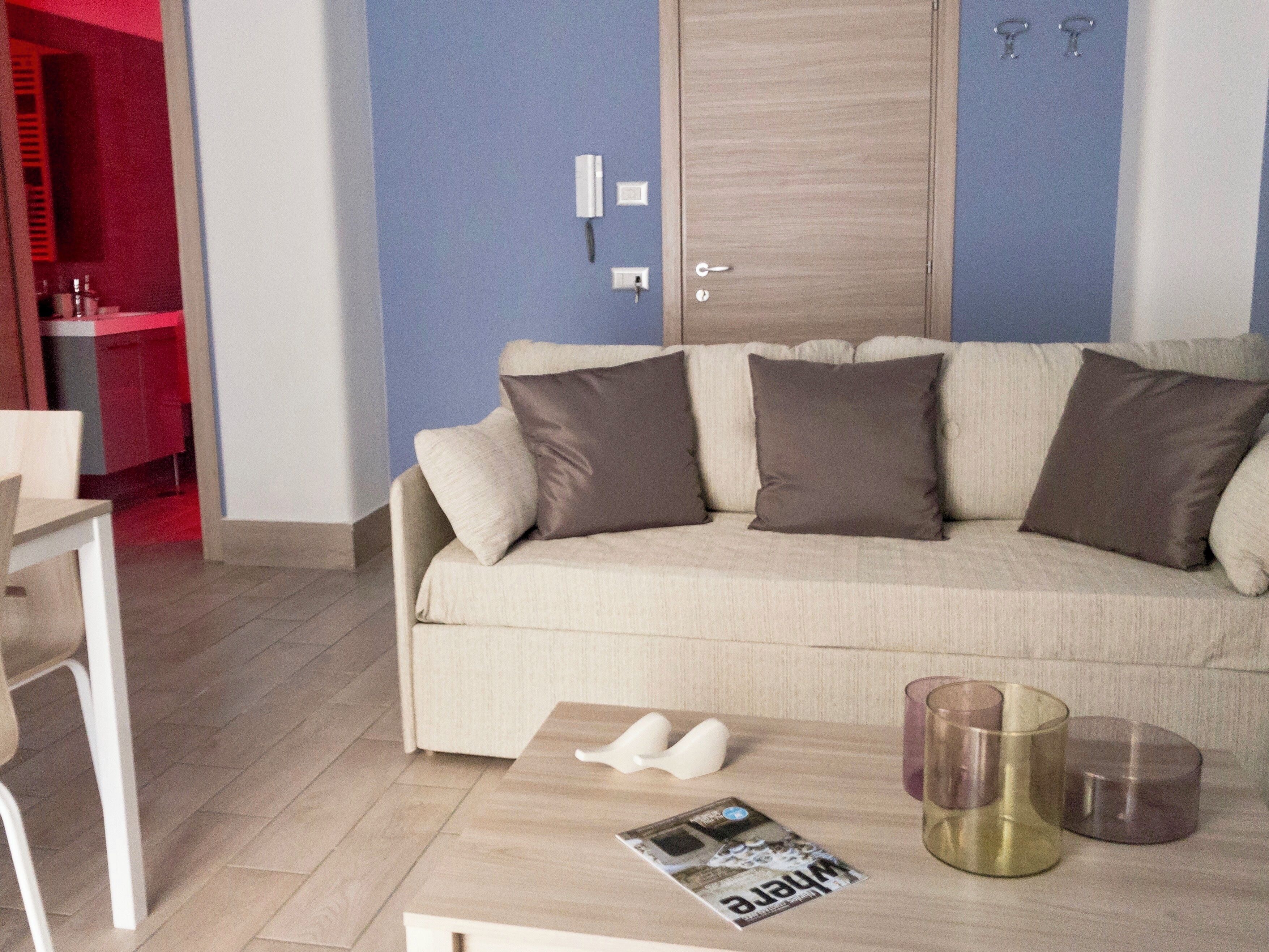 A living room with a beige sofa, two cushions, a coffee table with a magazine, and a door with a key lock.