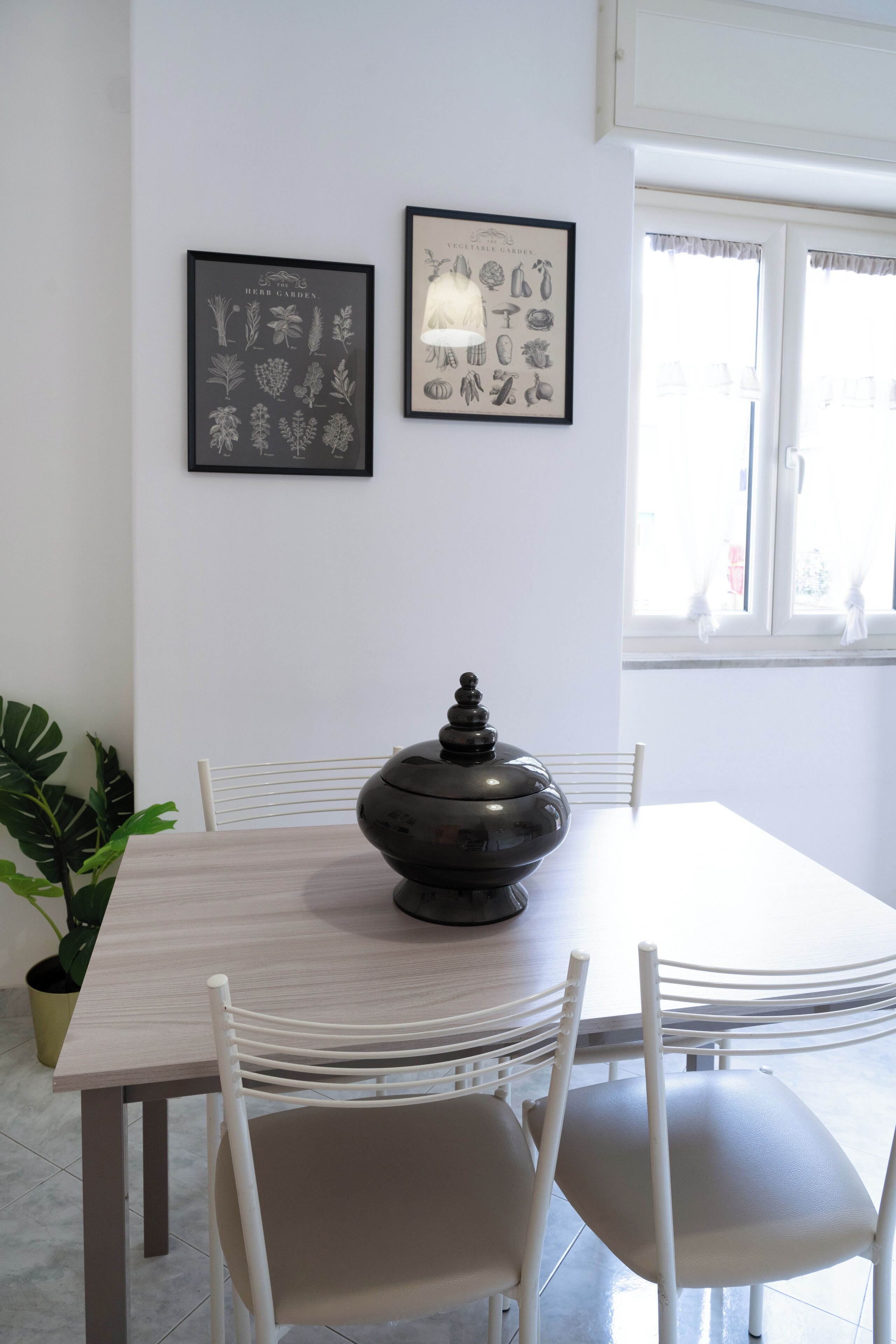 A dining area with a table, chairs, a decorative bowl, and two framed botanical prints on the wall.