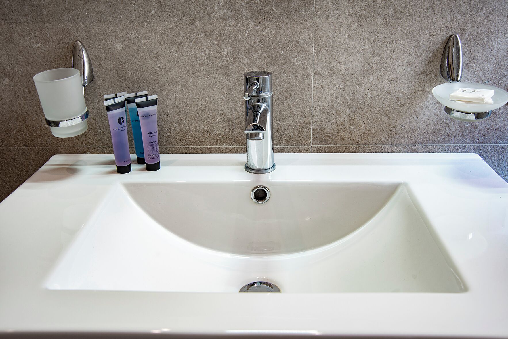 Een wit badkamermeubel met een moderne kraan, twee zeepdispensers en een zeephouder aan de muur.