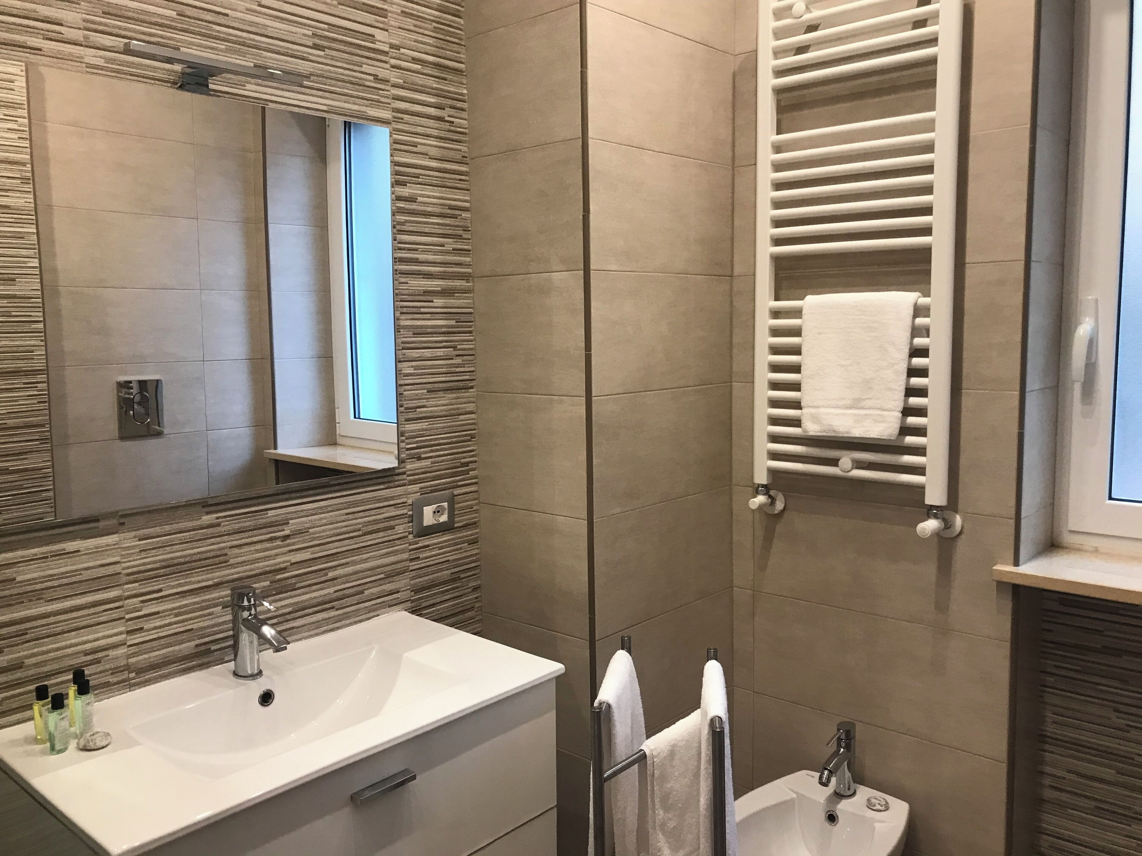 A modern bathroom with a large mirror, a sink with a vanity, a towel rack, and a shower area.