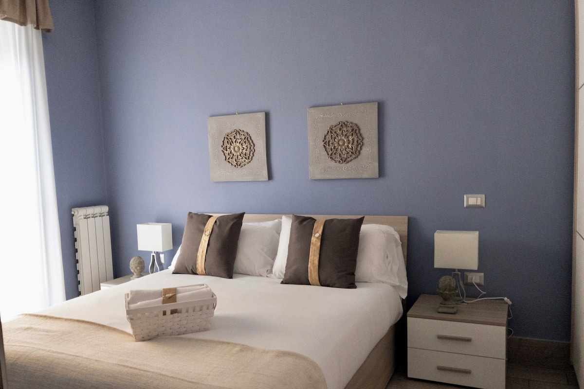 Una habitación de hotel con una cama, dos lámparas de pared, una mesita de noche y un radiador.
