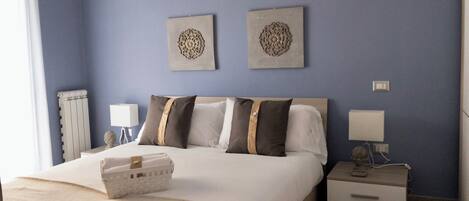 A hotel room with a bed, two wall-mounted lamps, a nightstand, and a radiator.