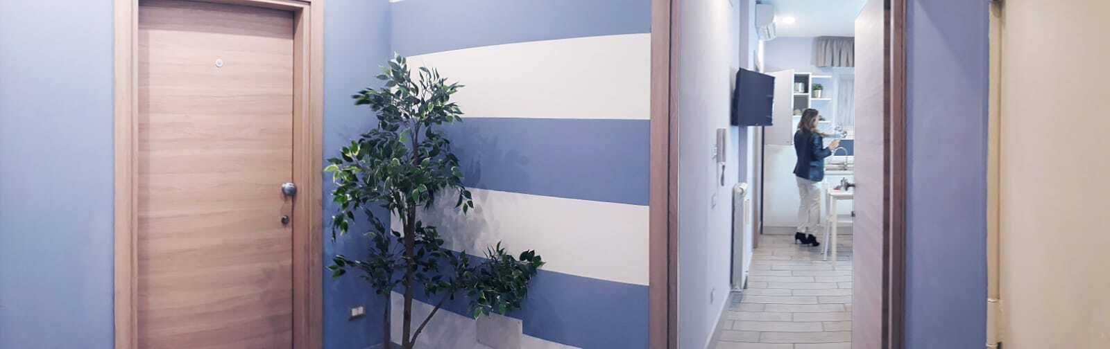A hallway with a wooden door, a potted plant, and a person in the distance.