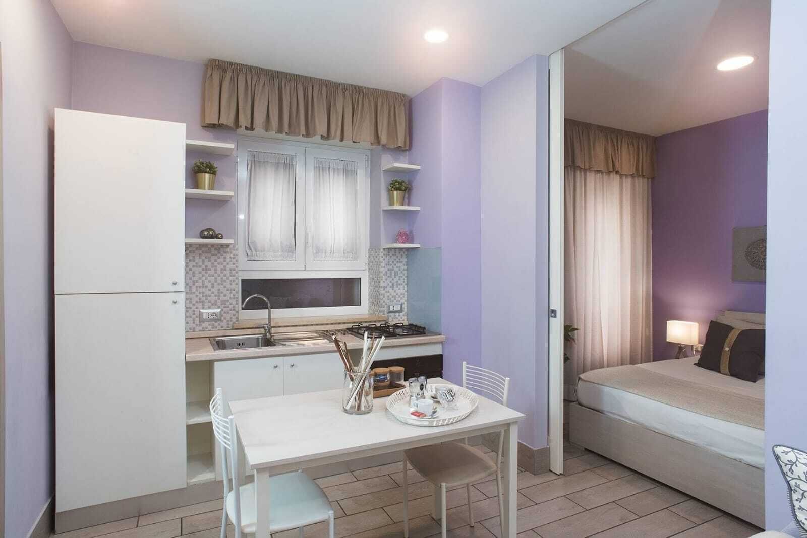 Une cuisine compacte avec un coin repas, un lit et une salle de bain visible à travers une porte ouverte.