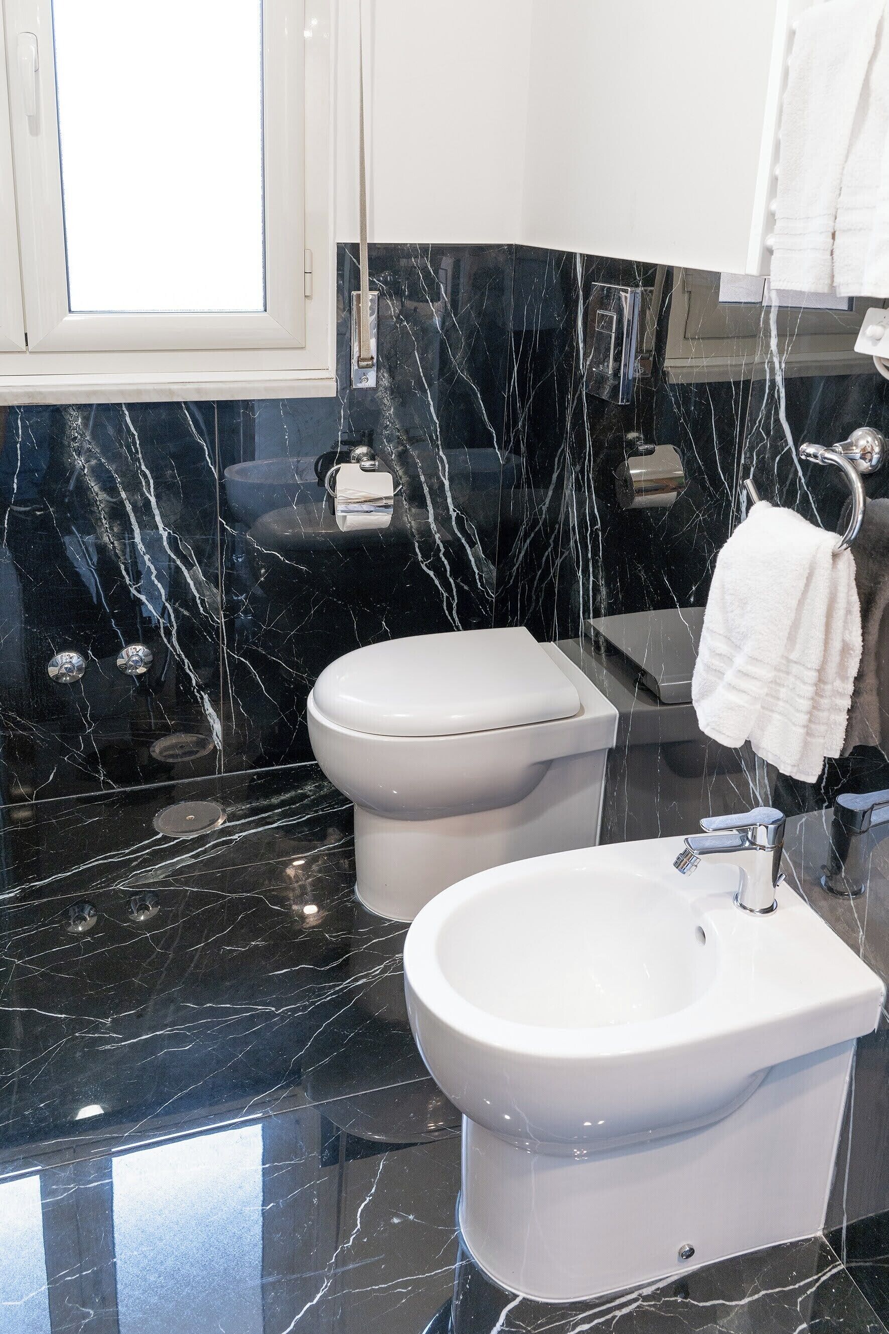 A modern bathroom with a black marble vanity, a white toilet, and a bidet.