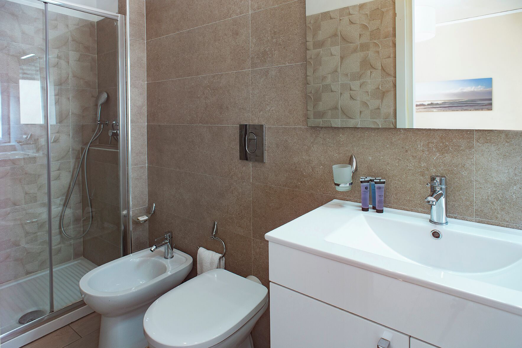 Une salle de bain équipée d’une douche, d’un bidet, de toilettes, d’un lavabo et d’un miroir agrémenté d’une image.