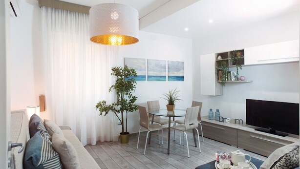 A modern living room with a sofa, a dining table with chairs, a potted plant, and a television. - Residenza Flegrea (Naples)