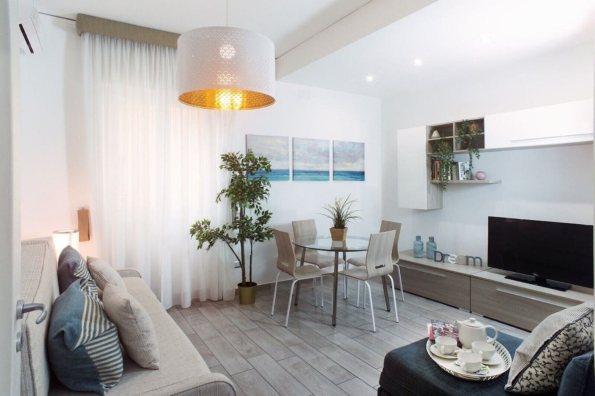 Una sala de estar moderna con un sofá, una mesa de comedor con sillas, una planta en maceta y un televisor.