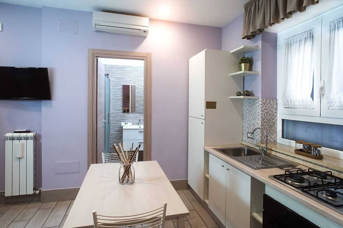 Cocina compacta con mesa de comedor, estufa integrada y televisor sobre la encimera.