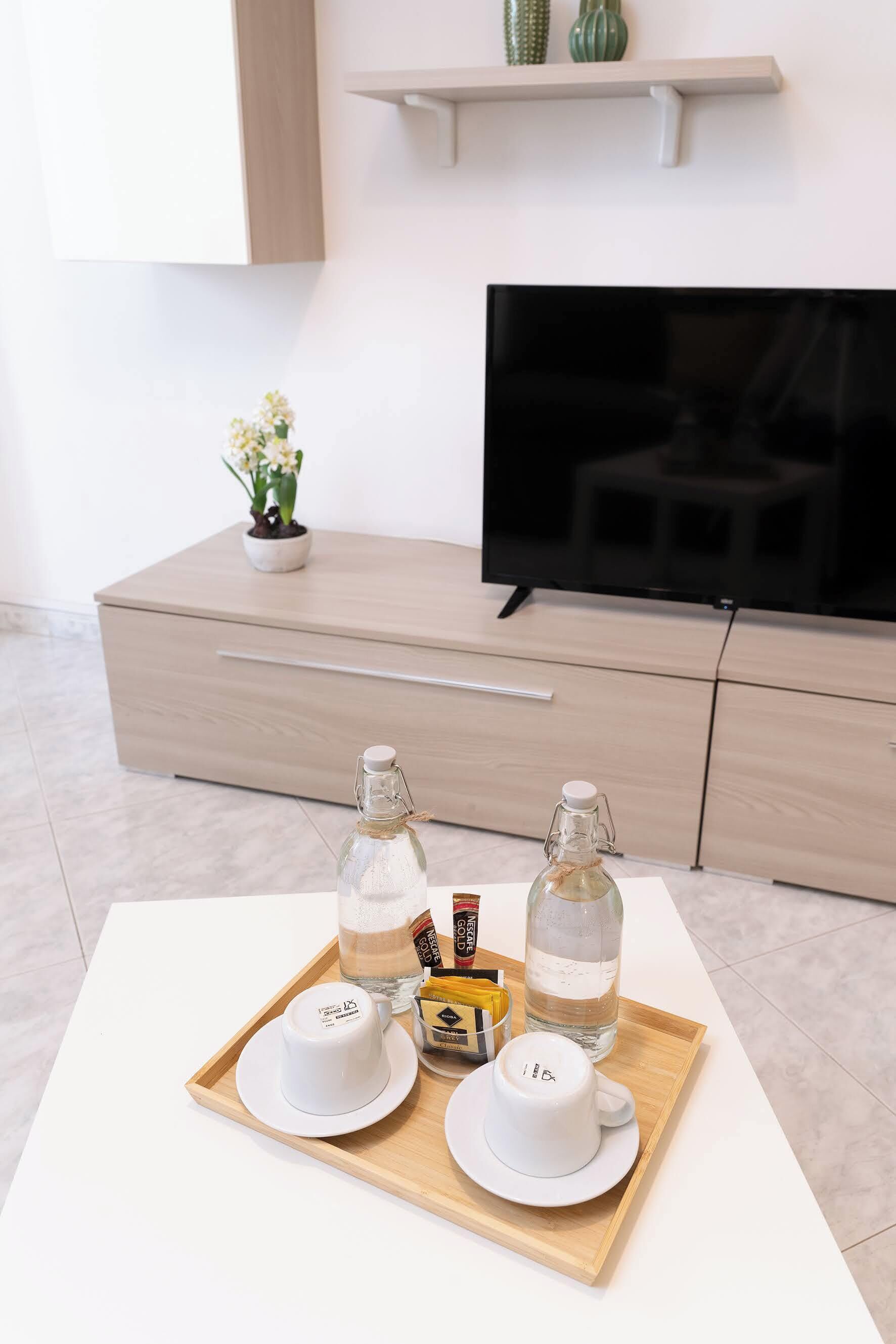 A modern living room with a white coffee table, a tray with two white cups, a bottle of water, and a small plant.