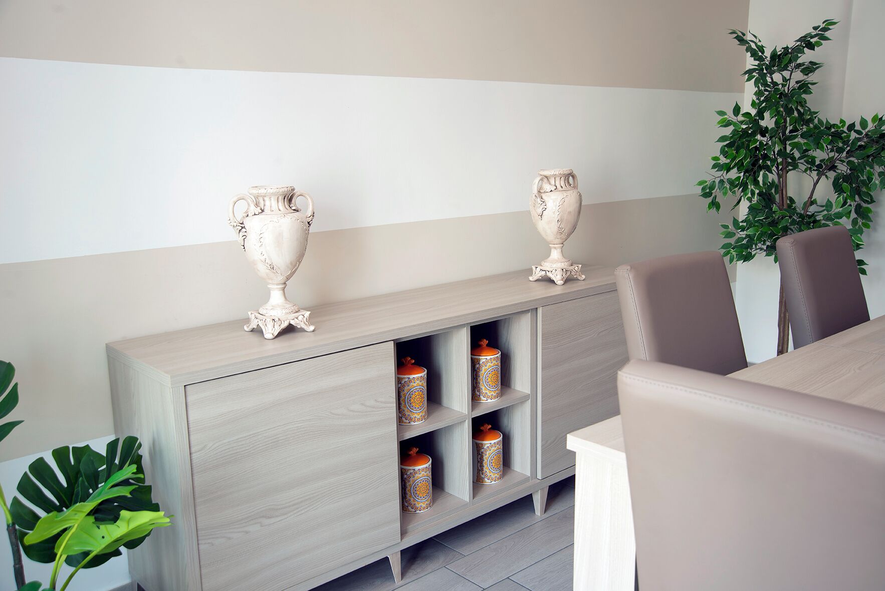 A modern living room with a light wood cabinet, two decorative vases, and a potted plant.