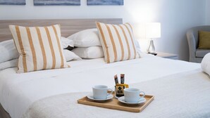 A neatly made bed with striped pillows, a tray with two cups and a bottle, and artwork on the wall. - Residenza Flegrea (Naples)