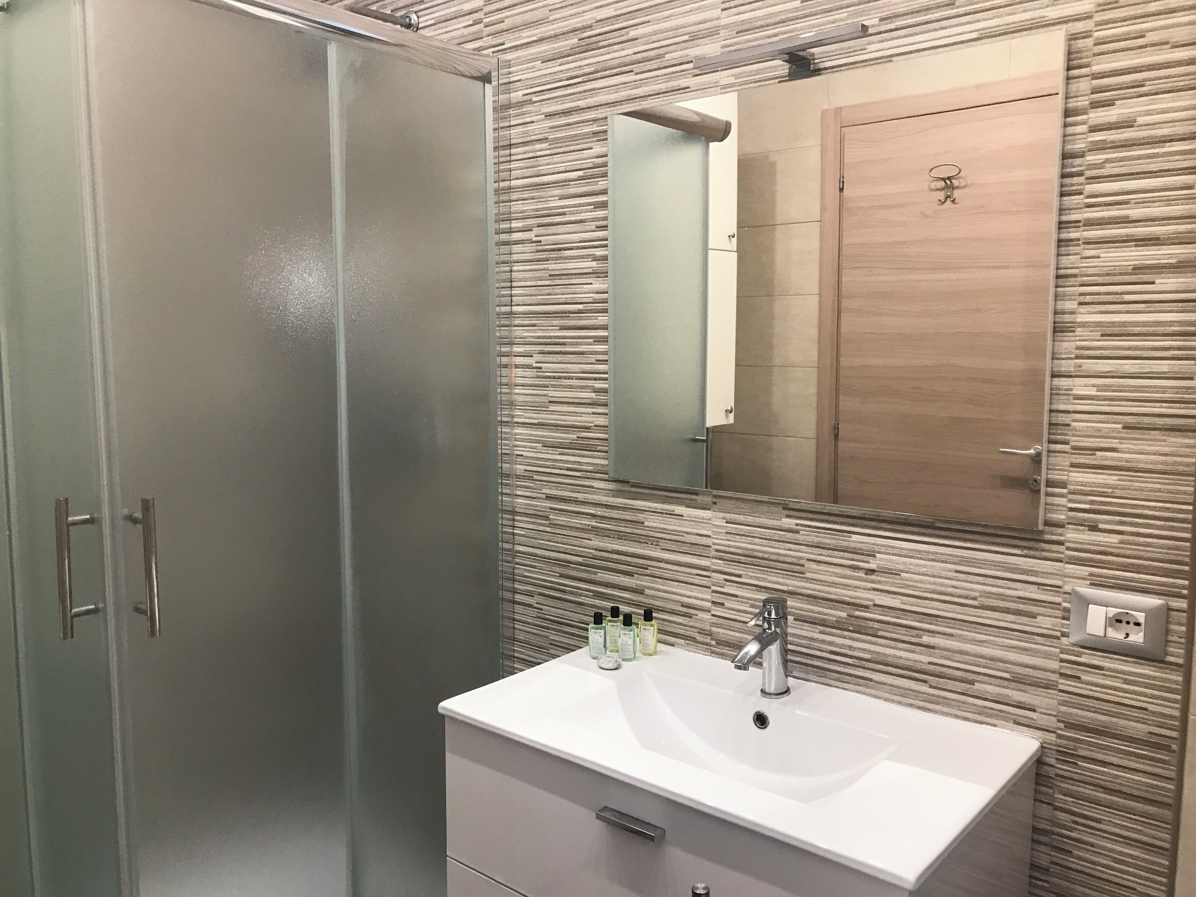 A bathroom with a modern design, featuring a large mirror, a white sink, and a wooden cabinet.