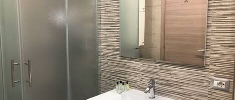 A bathroom with a modern design, featuring a large mirror, a white sink, and a wooden cabinet.