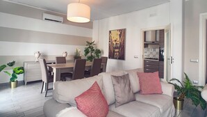 A modern living room with a sofa, dining table, chairs, and a kitchen area. - Residenza Flegrea (Naples)