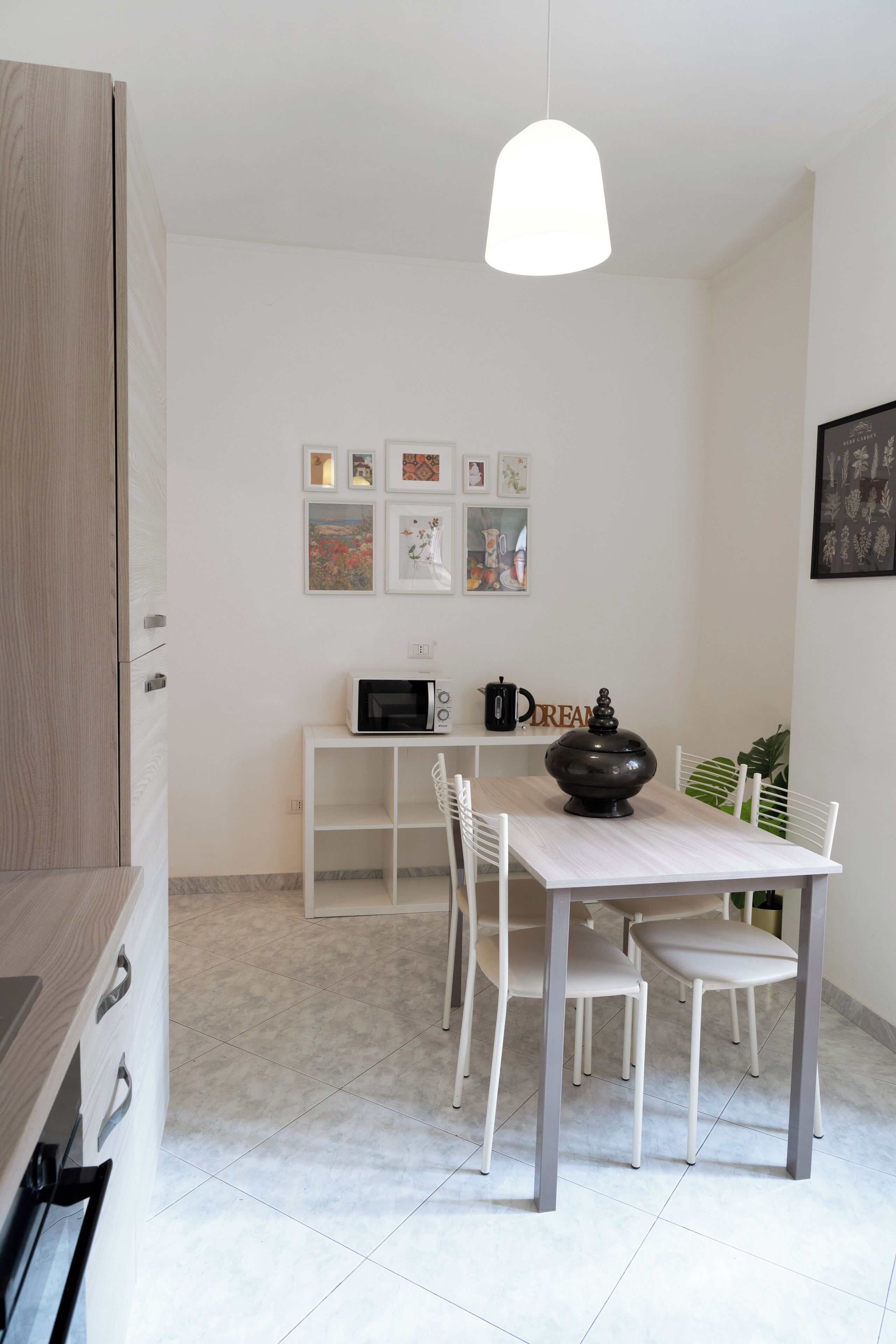A modern kitchen with white cabinetry, a dining table with chairs, a microwave, a coffee pot, and a decorative bowl.