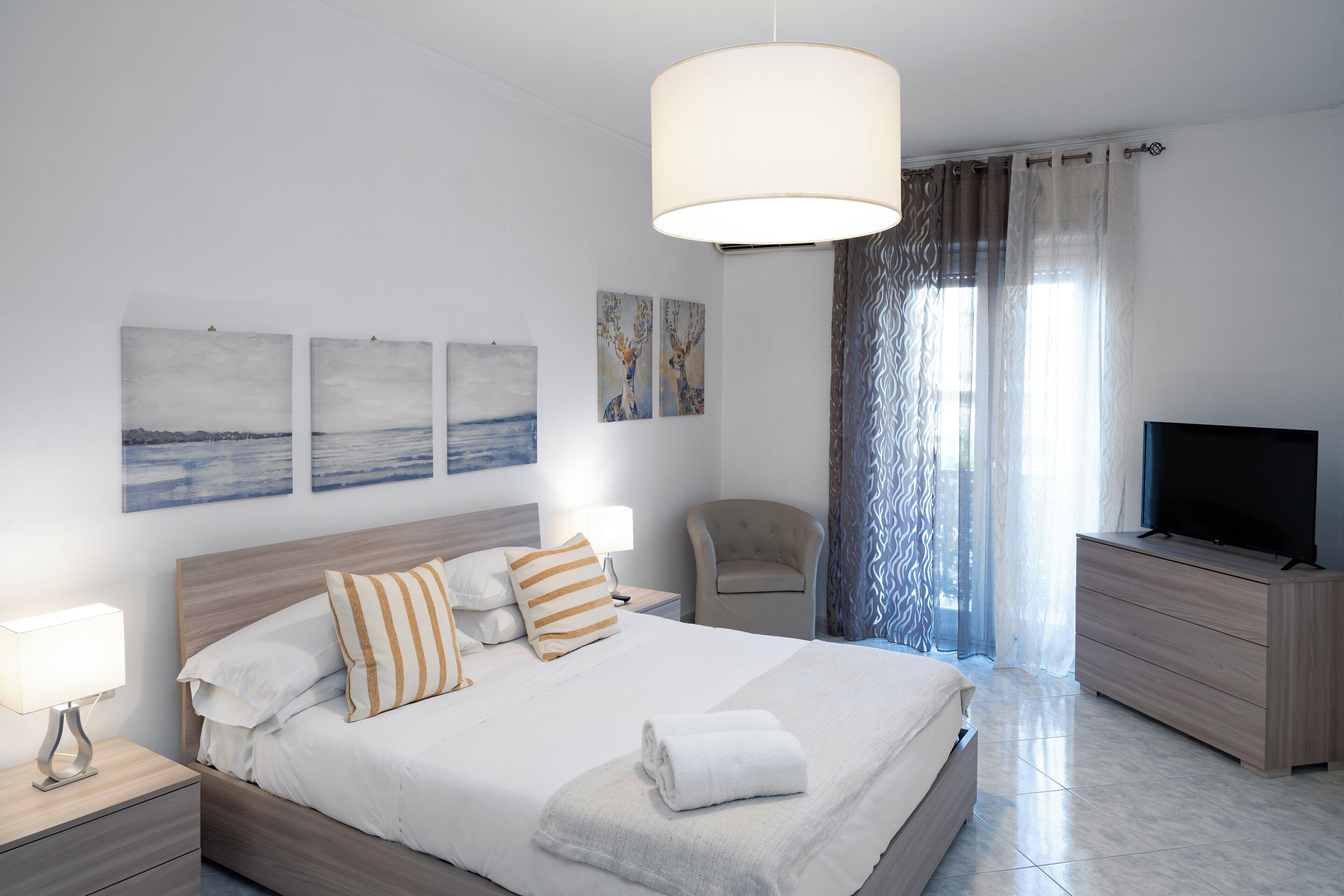 A modern hotel room with a large bed, a television, a chair, and artwork on the walls.