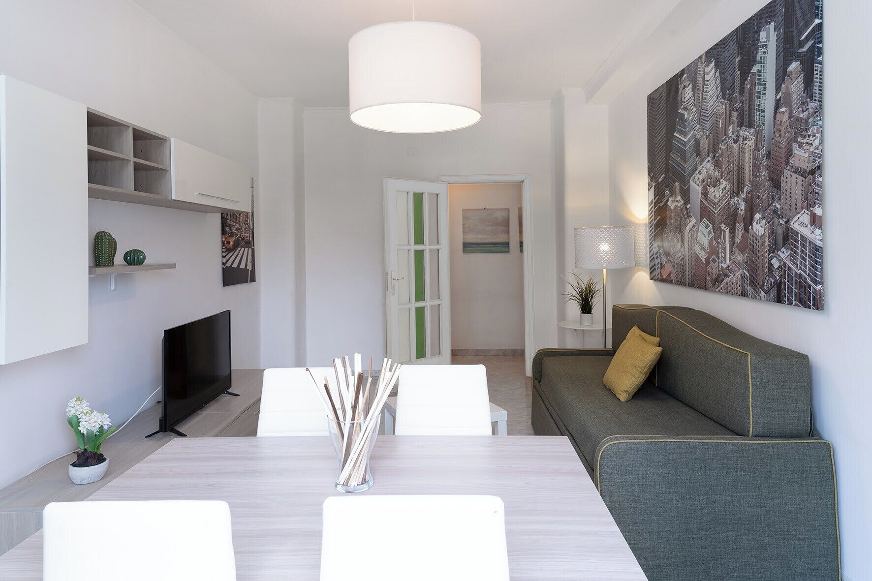 A modern living room with a dining table, sofa, TV, and artwork.