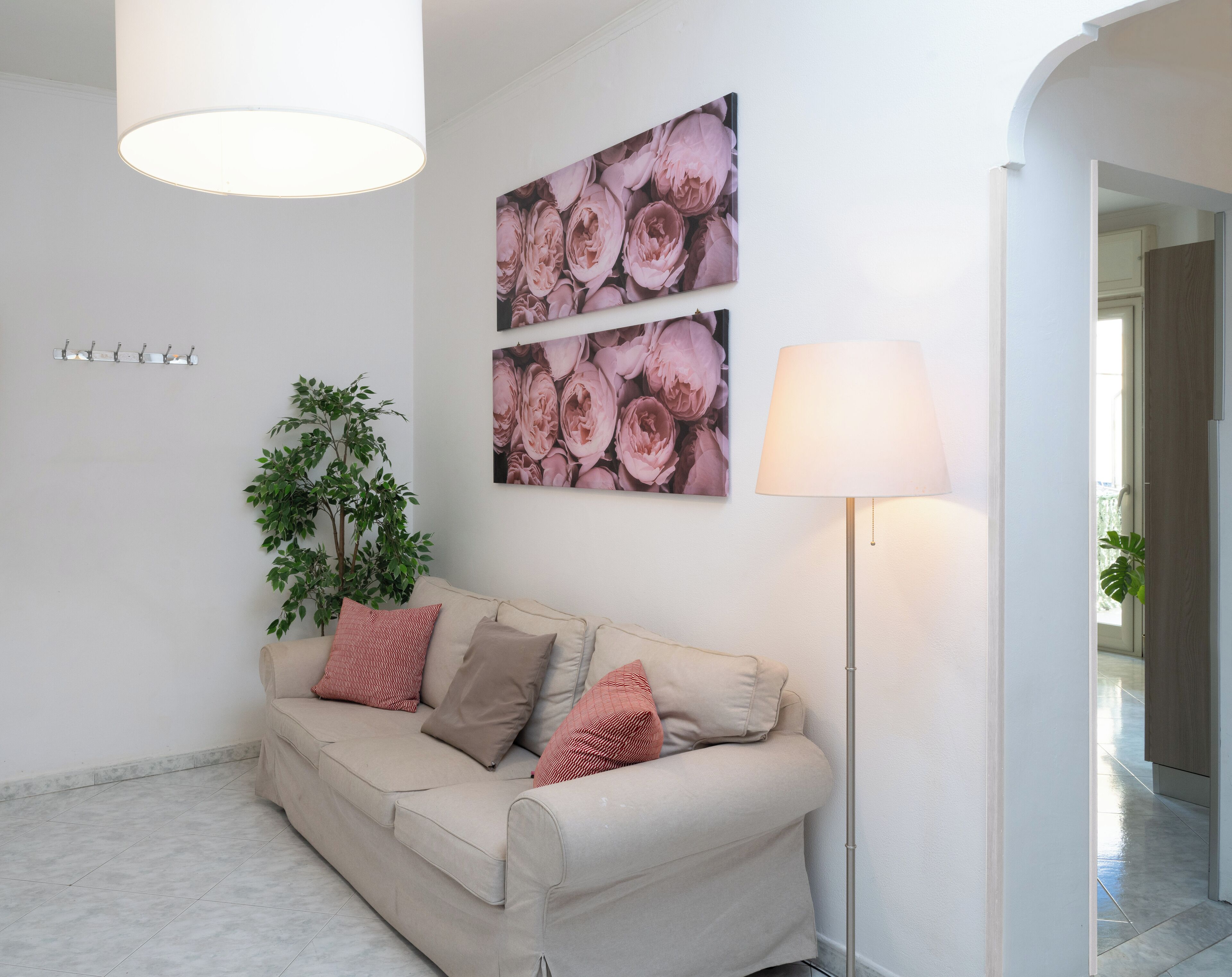 A modern living room with a beige sofa, a floor lamp, and a wall-mounted picture of pink flowers.