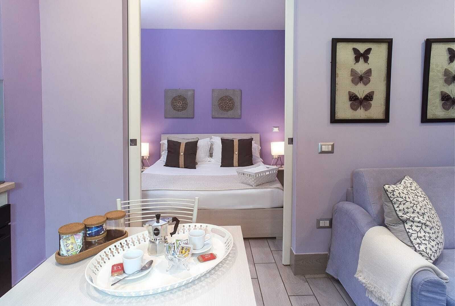 A bedroom with a bed, bedside tables, a nightstand, a tray table with breakfast items, and framed butterfly art on the wall.
