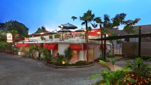 A hotel with a red and white facade, outdoor seating area with umbrellas, and a landscaped garden. - favehotel Sudirman Bojonegoro (Bojonegoro)
