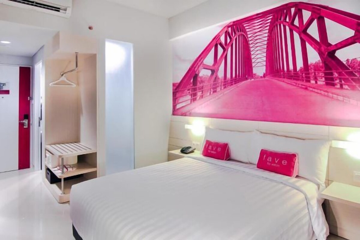 A hotel room with a bed, a wardrobe, a hanging closet, and a large pink bridge artwork on the wall.